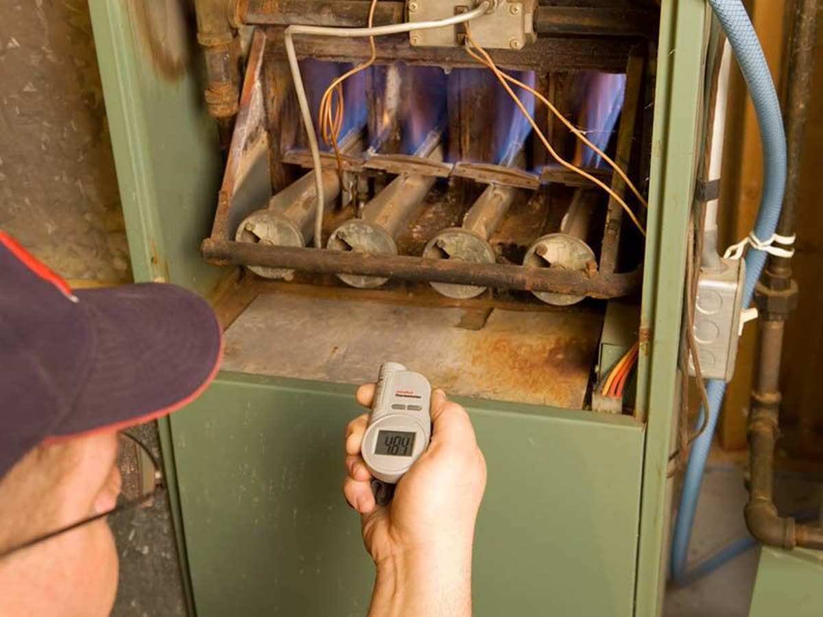 A technician checking the burners of a gas furnace with a handheld meter
