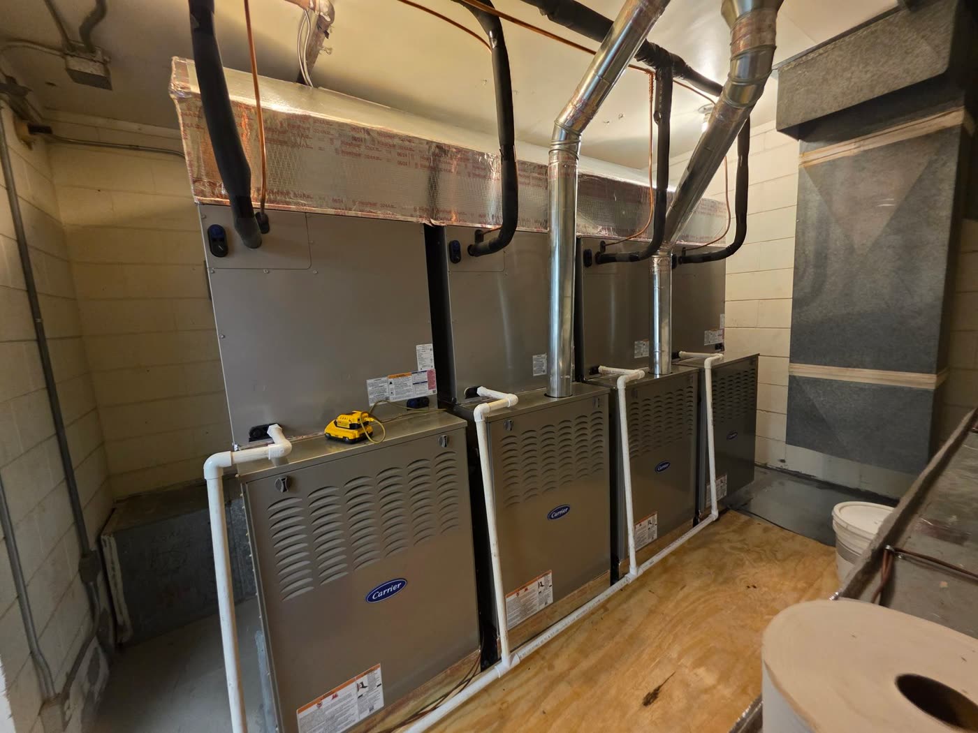 Three new Carrier gas furnaces standing side by side in one mechanical room, with new flues and copper lines