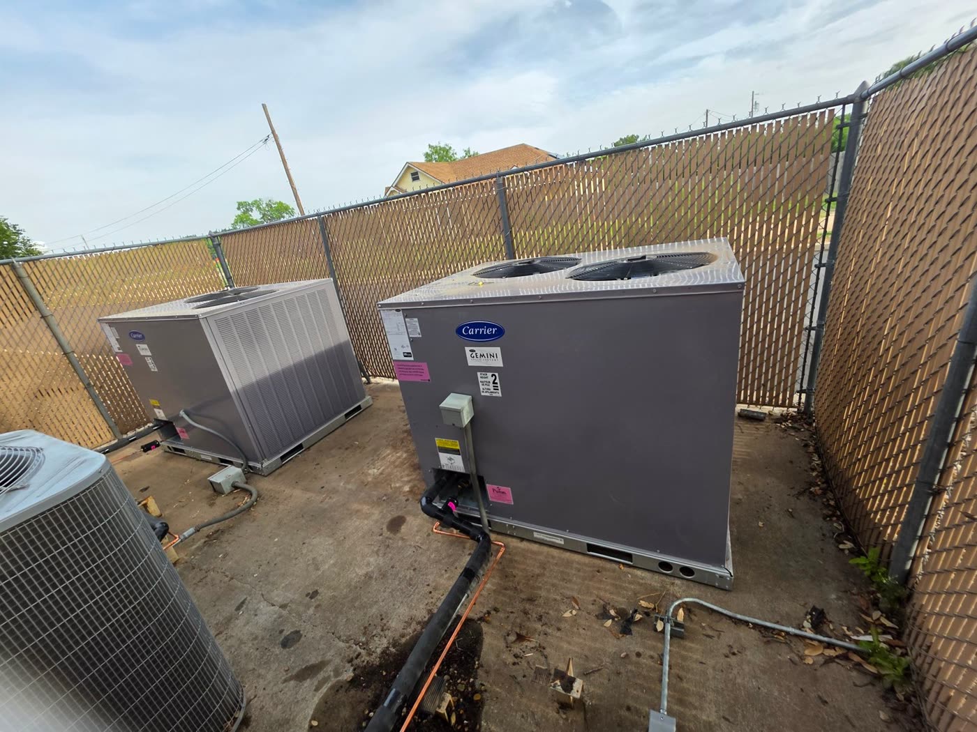 Two Carrier rooftop-style package units behind a privacy fence at a commercial site
