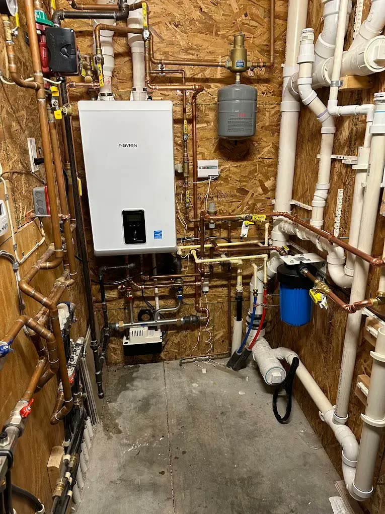 A Navien tankless water heater mounted on a plywood wall with new copper and PVC lines